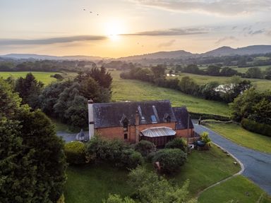 A countryside house with a glass conservatory surrounded by greenery and a driveway at Owlbury Hall Barn in Snead near Bishops Castle Montgomery