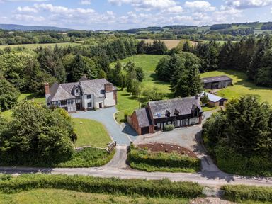 An aerial view of two houses with driveways and lawns surrounded by trees and fields at Owlbury Hall Barn in Snead near Bishop's Castle Montgomery