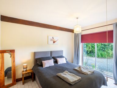 A bedroom with a double bed next to a large window with red blinds and a wooden floor mirror at Owlbury Hall Barn in Snead near Bishops Castle Montgomery