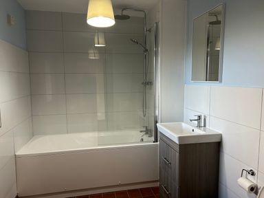 A bathroom with a bathtub with shower and glass screen a sink with cabinet and a mirror above at Owlbury Hall Barn in Snead near Bishops Castle Montgomery