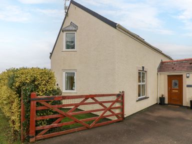 The exterior of a cream colored house with two windows a wooden front door and a red wooden gate at Ocean House in Broad Haven