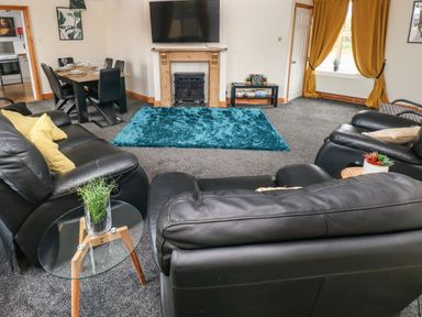 A living room with black leather sofas a blue rug a wooden fireplace and a dining table with chairs at Ocean House in Broad Haven