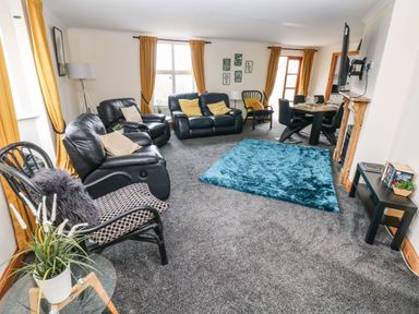 A living room with black leather sofas a blue rug a dining table and mustard curtains at Ocean House in Broad Haven