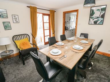 A dining room with a wooden table set for six and black chairs at Ocean House in Broad Haven