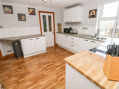 A kitchen with white cabinets wooden floor and knives in a block at Ocean House Broad Haven