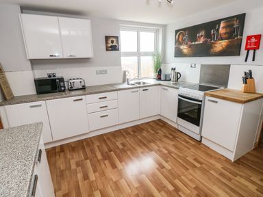A kitchen with white cabinets wooden floor microwave toaster stove and window at Ocean House in Broad Haven