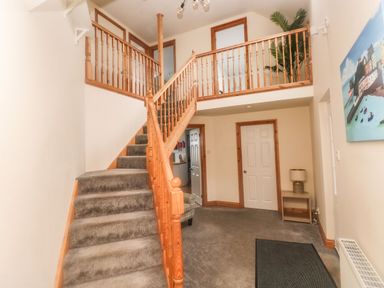 A hallway with carpeted stairs and wooden railing with a console table and lamp at Ocean House in Broad Haven