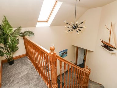 A staircase with wooden railing a skylight light fixture a potted plant a model sailboat on a shelf and a painting on the wall at Ocean House in Broad Haven