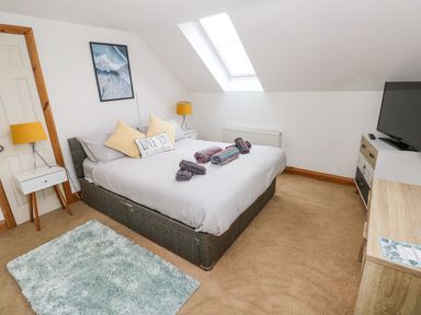 A bedroom with a double bed towels on the bed two bedside tables with lamps a skylight window a dresser with a television and a rug on the floor at Ocean House in Broad Haven
