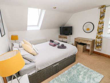 A bedroom with a bed towels a TV on a dresser a desk with a stool and a window with curtains at Ocean House in Broad Haven