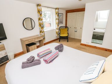 A bedroom with a bed topped with folded towels a wooden desk a round wall mirror a black chair with a yellow cushion a wardrobe with double doors and a long rectangular mirror on the wall at Ocean House in Broad Haven