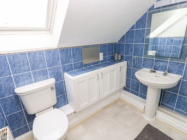 A bathroom with a toilet sink mirror and cabinet under a slanted ceiling at Ocean House in Broad Haven
