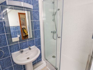 A bathroom with a white sink and a glass enclosed shower with blue tiled walls at Ocean House in Broad Haven