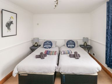 A bedroom with two single beds side by side with pillows and towels bedside tables with lamps and wall art at Ocean House in Broad Haven