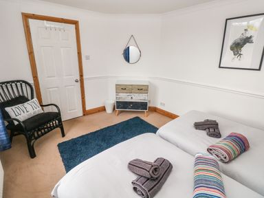 A bedroom with two single beds with towels a black chair with a pillow white door a small dresser and a round mirror on the wall at Ocean House Broad Haven