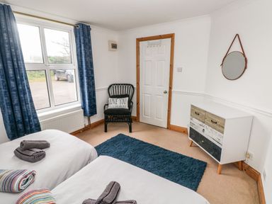 A bedroom with two beds a black chair a dresser and a round mirror at Ocean House in Broad Haven