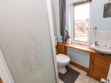 A bathroom with a toilet sink shower and window with curtain at Ocean House in Broad Haven