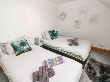 A bedroom with two single beds with pillows and folded towels on white bedding at Ocean House in Broad Haven