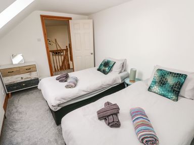 A bedroom with two single beds with rolled towels on each bed and a small dresser with a mirror at Ocean House in Broad Haven