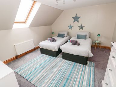 A bedroom with two single beds a striped blue rug and a skylight window at Ocean House in Broad Haven