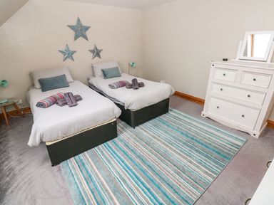 A bedroom with two single beds a striped rug a white chest of drawers and three star decorations on the wall at Ocean House in Broad Haven