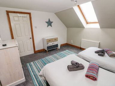 A bedroom with two single beds a skylight window a colorful striped rug a small chest of drawers and a door at Ocean House in Broad Haven