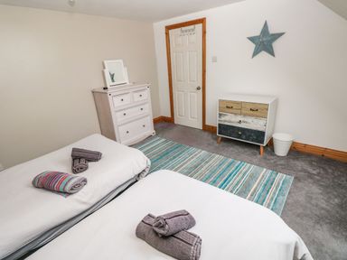 A bedroom with two single beds with towels on them a striped rug a chest of drawers a door and a star decoration on the wall at Ocean House in Broad Haven