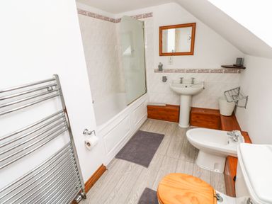 A bathroom with a bathtub shower combination pedestal sink bidet and toilet with a wooden seat at Ocean House in Broad Haven