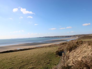 A coastal landscape with a sandy beach grassy fields and cliffs at Ocean House in Broad Haven