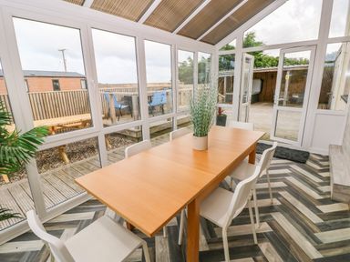 A dining area with a wooden table and white chairs in a glass sunroom at Ocean House in Broad Haven