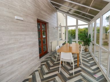 A sunroom with a wooden table and white chairs near a wooden door with glass panes at Ocean House in Broad Haven