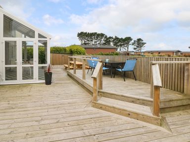 A wooden deck with blue chairs around a table and a picnic table next to a white conservatory at Ocean House in Broad Haven