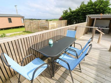 An outdoor seating area with a black table and four blue chairs on a wooden deck at Ocean House in Broad Haven