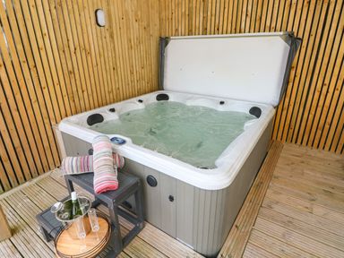 A hot tub with water inside and striped towels on a small black table with champagne and glasses in a wooden room at Ocean House in Broad Haven