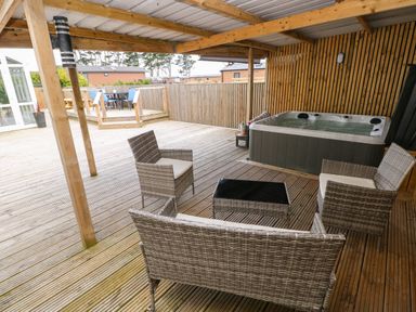 A covered wooden deck with wicker furniture and a hot tub at Ocean House in Broad Haven