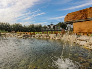 A wooden water spout flowing into a pond with rocks and a house in the background at Fairview Lodge in Pwllheli