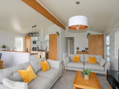 A living room with two gray sofas and yellow cushions a wooden coffee table and kitchen area at Fairview Lodge in Pwllheli