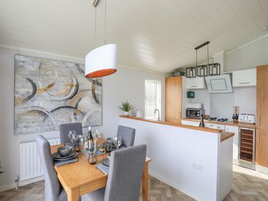 A dining area with a wooden table set for four next to a kitchen with wooden cabinets at Fairview Lodge in Pwllheli