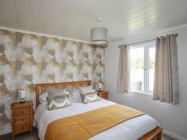 A bedroom with a wooden bed between two wooden nightstands with lamps and a window with curtains at Fairview Lodge in Pwllheli