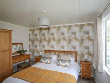 A bedroom with a bed a wooden dresser with a mirror two bedside tables with lamps and a window at Fairview Lodge in Pwllheli