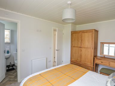 A bedroom with a bed covered by a yellow blanket a wooden wardrobe a dressing table with a mirror and an open door showing a bathroom at Fairview Lodge in Pwllheli