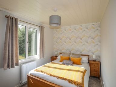 A bedroom with a bed with yellow and gray pillows and a yellow blanket between two wooden nightstands with lamps at Fairview Lodge in Pwllheli