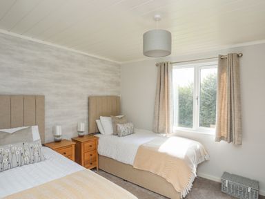 A bedroom with two single beds bedside tables and a window with curtains at Fairview Lodge in Pwllheli
