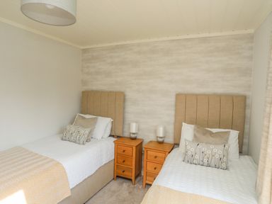 A bedroom with two single beds separated by two wooden bedside tables with lamps at Fairview Lodge in Pwllheli