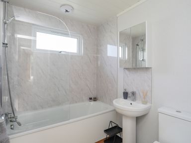A bathroom with a bathtub shower combination a pedestal sink a mirrored cabinet and a toilet at Fairview Lodge in Pwllheli