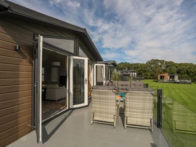 A patio with outdoor chairs and table next to a building with open glass doors overlooking a grassy area at Fairview Lodge in Pwllheli
