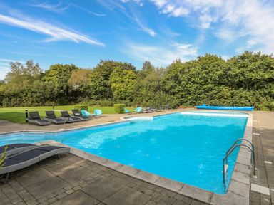 An outdoor swimming pool with lounge chairs and blue sky at Fairview Lodge in Pwllheli