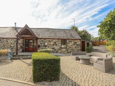 An outdoor area with stone building labeled reception and wicker patio furniture at Fairview Lodge in Pwllheli
