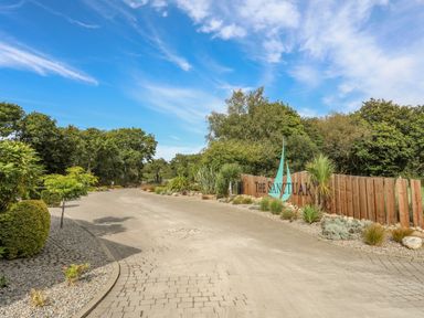 An entrance road with landscaping and a wooden sign that reads The Sanctuary surrounded by trees at Fairview Lodge in Pwllheli