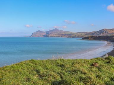 A coastal landscape with grassy foreground beach and mountains in the distance at Fairview Lodge in Pwllheli